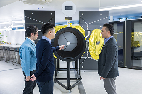 衛星モデルを前に仲間と宇宙技術について語る